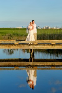 bride and groom posing by water with ocean city skyline in background